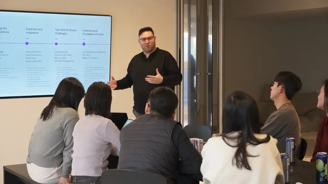 A man presents information on a screen to a seated group in an office. They appear engaged and attentive.