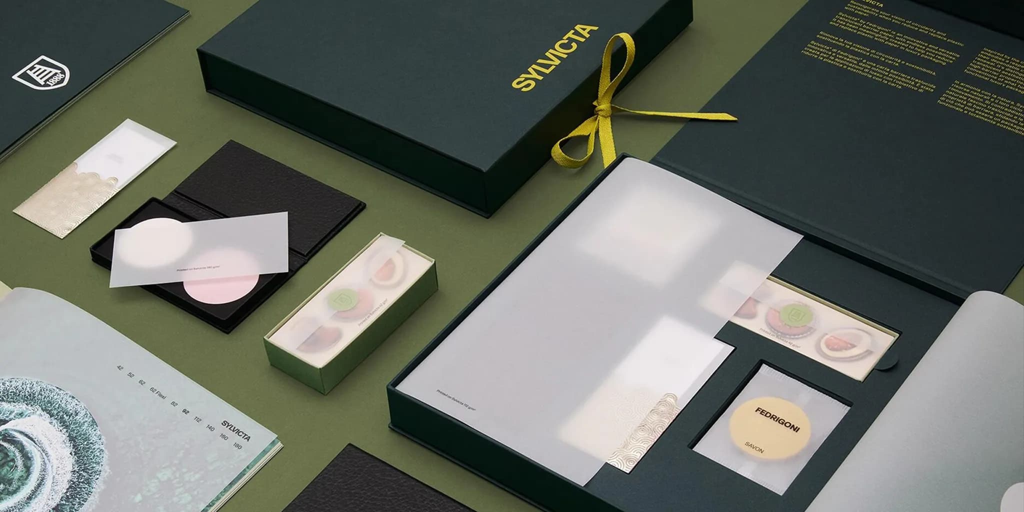 Elegant stationery set with dark green boxes, gold lettering, and included samples arranged on a green surface.