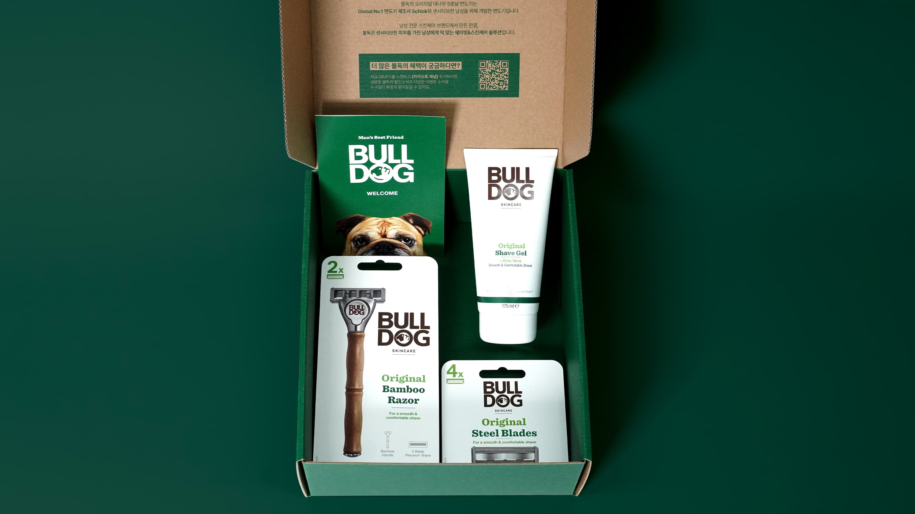 Open box with Bulldog skincare and shaving products: razor, blades, and shave gel, on a green background.