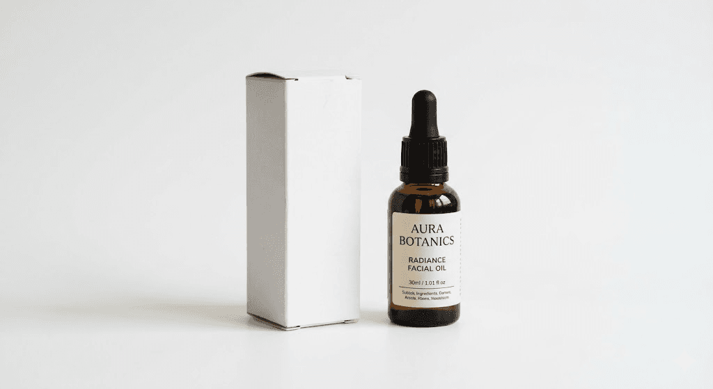 Brown bottle of Aura Botanics Radiance Facial Oil with dropper, next to a plain white box, on a white background.
